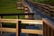 Wooden boardwalk over marshland lit by sunlight in the golden hour.