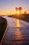 Wooden boardwalk at sunrise, lone figure walking a dog, with sun beams and palm trees, Sa Coma, Mallorca, Spain