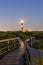 Wooden boardwalk trail illuminated by a tall lighthouse beacon at night