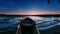 Wooden boat at the lake shore with rolling waves on it in the foreground and sunset sky with spindrift clouds on horizon