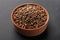 Wooden bowl of coriander grains on dark background