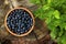 Wooden bowl of delicious bilberries and green leaves on stump, flat lay