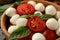 Wooden bowl with mozzarella, tomato and basil, close up