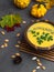 wooden bowl of traditional pumpkin soup on gray table, decorated with seeds, parsley, colorful foliage, decorative pumpkin