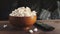Wooden bowl of white salty popcorn and remote control on a wooden table in front of a couch. Front view, blurry