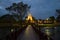 The wooden bridge conducting to ruins of the ancient Buddhist temple of Wat Sa Si in evening twilight. Sukhothai, Thailand