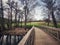 Wooden bridge extends over a tranquil pond, leading to a lush and verdant park