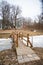 Wooden bridge over a frozen river in the park with lighting lanterns and wooden protective barriers. In the background you can see