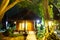 Wooden bungalow in the forest. House at night in the jungle. Tall green tropical trees in the foreground, in the background a