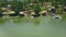 Wooden bungalows with thatched roof and boat pier on shore green lake in resort hotel drone view. Cottages on shore