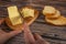 Wooden butter dish with a piece of butter and slices of cheese and fresh wheat toast on a wooden background. Someone cuts off a