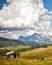 A wooden cabin in a green land under white clouds with the beautiful mountains in the background