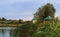 wooden cabin near the edge of a small small river or pond amidst lush foliage nearing sunset.