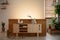 Wooden cabinet with candles and vases surrounded by plants in a natural living room interior. Real photo. Empty wall, place your p