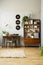 Wooden cabinet next to chair at desk in vintage home office interior with vinyl and lamp. Real photo