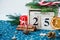 Wooden calendar with 25 December date in it on green place mat, candle, fir tree, dried oranges, pines. Christmas celebration