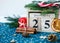 Wooden calendar with 25 December date in it on green place mat, candle, fir tree, dried oranges, pines. Christmas celebration