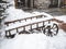 A wooden cart covered with snow stands in a snowdrift next to a stone building with marble steps