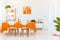 Wooden chairs at table in white and orange dining room interior with poster and plant