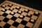 Wooden checkerboard with game pieces on black table, closeup