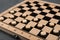 Wooden checkerboard with game pieces on grey table, closeup