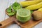 On a wooden chopping board with a light background the Ingredients spinach, buttermilk, kiwi and banana for a tasty smoothie.