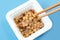 Wooden chopsticks holding Japanese natto beans on blue background top view.