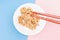 Wooden chopsticks holding japanese natto beans on pink and blue background top view.