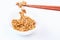 Wooden chopsticks holding japanese natto beans on white background.