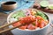 Wooden chopsticks with piece of salmon over delicious poke bowl on table, closeup