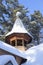 Wooden Christian bell tower with a dome and a cross covered with snow in the forest in winter