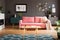 Wooden coffee table with tea cup and open book standing on carpet in dark living room interior with powder pink lounge with fur c