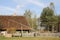 A wooden cottage in an open-air museum, with a well and a garden with flowers, a wooden fence