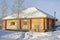 Wooden Country small house of timber stained yellow, snowy winter, sunny day.