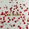 Wooden craft letters that spell Be Mine with red heart confetti on a white background