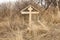 A wooden cross on an abandoned grave overgrown with dry grass
