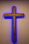 Wooden cross illuminated from neon purple LED strip hangs on a white wall in a church