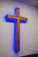 Wooden cross illuminated from neon purple LED strip hangs on a white wall in a church