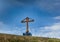 Wooden cross stands on a hill on a background of sky.