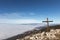 A wooden cross on top of Subasio mountain, with a sea of fog below and Assisi town (Umbria) in the background