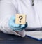 Wooden cube with a question mark in the doctor`s hand on a blue background. The concept of finding an answer to questions