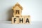 Wooden cubes form the word `FHA, federal housing administration` near miniature house. Beautiful white background, copy space.