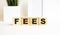 Wooden cubes with letters on a white table. The word is FEES. White background