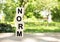 Wooden cubes are stacked vertically on a wooden table in the garden. The word NORM is written in black letters.