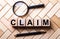 Wooden cubes with the word CLAIM stand on a wooden background between a magnifying glass and a handle