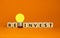 Wooden cubes with word `reinvest`. Yellow light bulb. Beautiful orange background. Business concept. Copy space