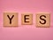 Wooden cubes with the word YES. Three wooden blocks with word YES on pink background. YES lettering on pink background