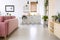 Wooden cupboard and pink sofa in bright flat interior with kitchenette and poster. Real photo