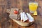 Wooden cutting board with crispbread, cheese, ham, cherry tomato, glass of fresh orange juice on a wooden background