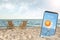 Wooden deck chairs on beach and smartphone with open weather forecast app